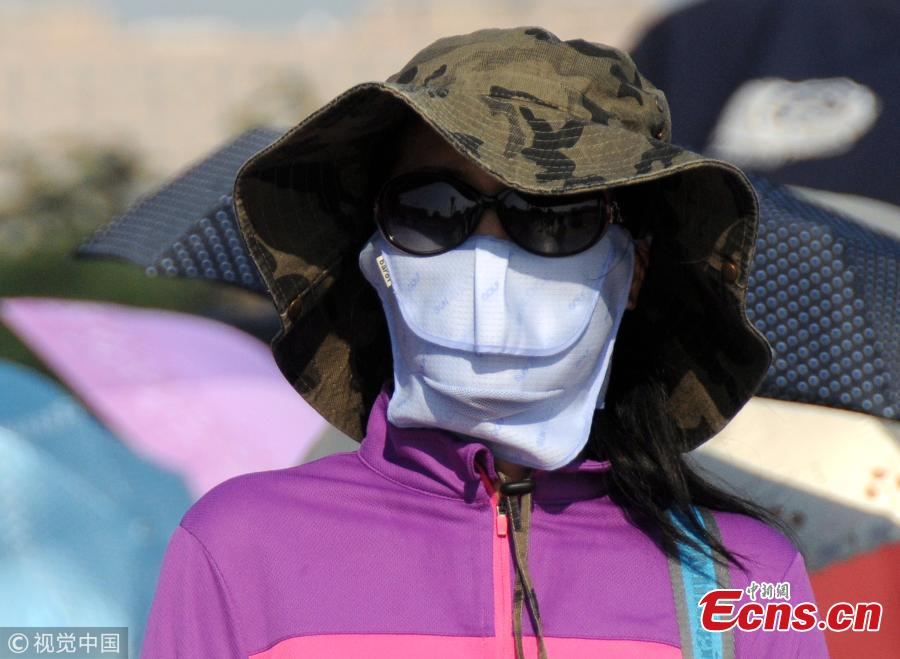 Tourists try all possible ways, including wearing hats, to shade themselves from the sun near the Forbidden City and Tiananmen Square in Beijing, March 31, 208, as temperatures rose to a record 35 degrees centigrade. Beijing issued a yellow alert against high temperatures on Thursday. (Photo/VCG)