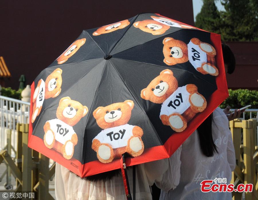 Tourists try all possible ways, including wearing hats, to shade themselves from the sun near the Forbidden City and Tiananmen Square in Beijing, March 31, 208, as temperatures rose to a record 35 degrees centigrade. Beijing issued a yellow alert against high temperatures on Thursday. (Photo/VCG)