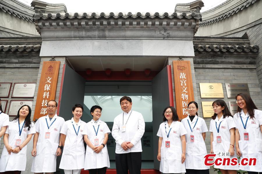 Shan Jixiang (C), the curator of the Palace Museum, poses with volunteers at the opening of its restoration \'hospital\' to the public in Beijing, June 9, 2018. As part of ongoing activities held for China\'s Cultural and Natural Heritage Day, the first batch of 40 people watched \'doctors\' repairing pieces from some of the museum\'s collections, including pieces of calligraphy, paintings, bronzeware and clocks, under the guidance of volunteers. Established in December 2016, the restoration hospital is located in the west of the Palace Museum. The facility covers 13,000 square meters and has the nation\'s most-advanced restoration studios. (Photo: China News Service/Liu Guanguan)