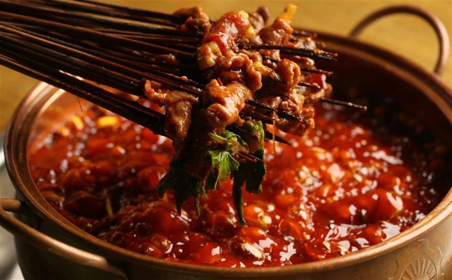 Chuanchuanxiang is a hot pot that cooks ingredients on skewers/sticks. (Photo/Shine.cn)
Chuanchuanxiang
Cooked and served in skewers, chuanchuanxiang can be described as one form of hotpot, or mini hotpot as some people call it. The word chuanchuan means sticks/skewers.
Originating in Chengdu, this spicy delicacy cooks all kinds of vegetable and meat skewers in hot spicy broth, just like hotpot but with skewers, and the cost of the meal is calculated by counting the number of skewers.
The chuanchuanxiang broth is filled with herbs and spices to elevate the depth of flavor, like caoguo (Amomum tsao-ko), fennel, baidoukou (Amomum kravanh), cloves and star anise. One can choose spicy or original broth, which has the same base of chicken or pork stock but different kinds and amount of seasonings.
Beef, shrimp, tofu and vegetables are the basic ingredients in chuanchuanxiang, and offal such as chicken heart, duck intestine and beef tripe are what makes a meal complete and authentic. When cooked in the spicy broth, the not-so-appetizing offal parts become mouthwatering delicacies.
Like hotpot, chuanchuanxiang is served with dipping sauces on the side. The traditional Sichuan flavor is made of a bowl of sesame oil-based sauce and a plate of dry ground chilies, toasted white sesame seeds and crushed peanuts.