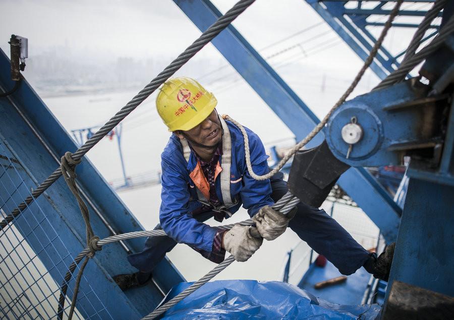 Yang Rengcai, 50, tries his best to fasten the main cable.[Photo/Xinhua]
