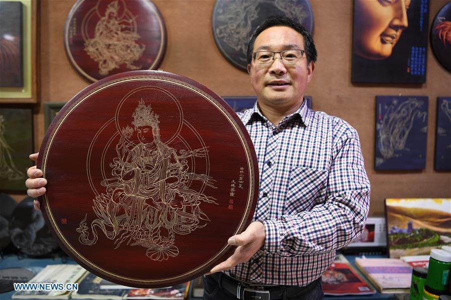 Shen Hongjie shows his woodcut work at his workshop in Dunhuang, northwest China\'s Gansu Province, May 6, 2019. In 2004, Shen Hongjie was impressed by Dunhuang culture as he came here for sightseeing. He then left his hometown in central China\'s Hunan Province for Dunhuang. For 15 years, Shen Hongjie has been dedicated to promoting Dunhuang culture through woodcut. (Xinhua/Fan Peishen)